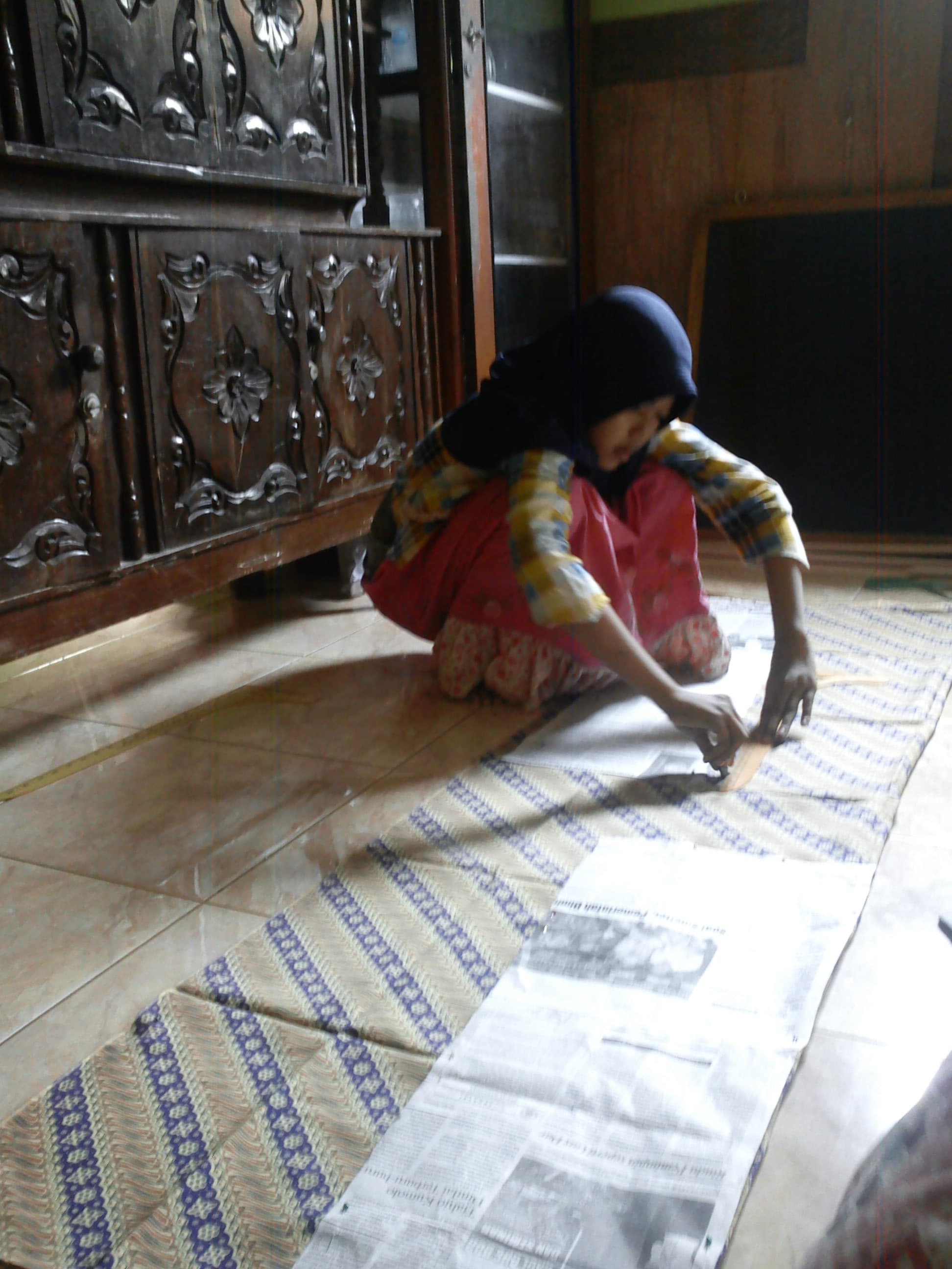 Mengukur kain dengan pola dari koran